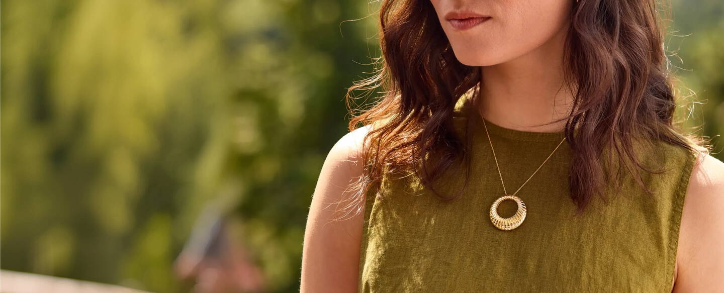A woman wearing a green shirt is wearing an open circle pendant of yellow gold.