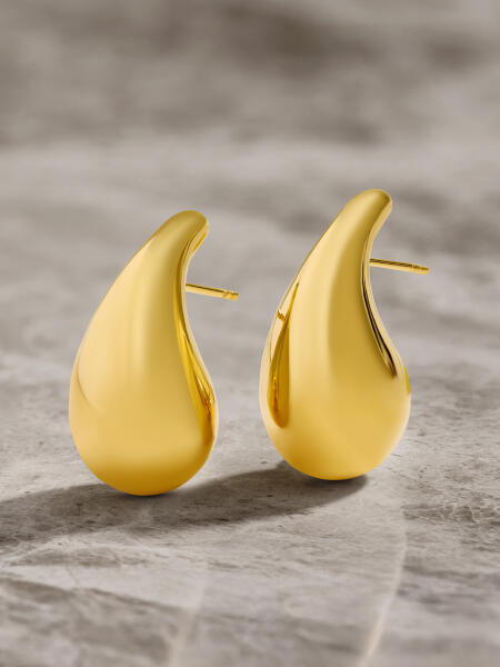 Teardrop earrings of yellow gold appear to float on a surface of gray marble.