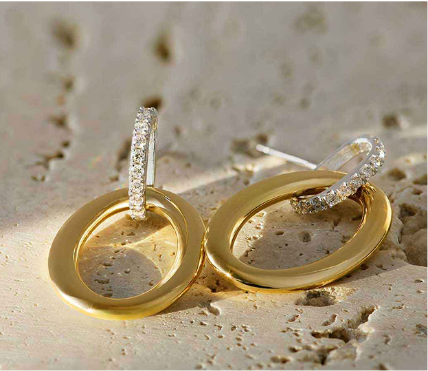18K yellow gold hoop earrings with diamonds rest on a textured beige stone surface.