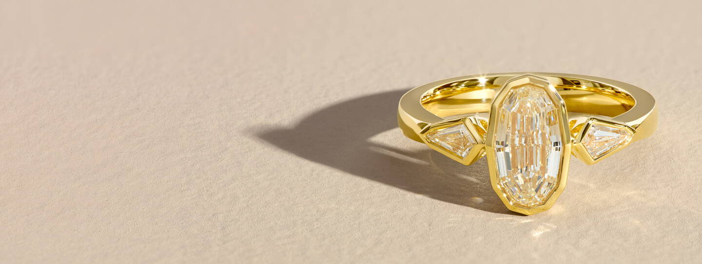 A bezel set oval diamond ring with two natural accent diamonds set in yellow gold.