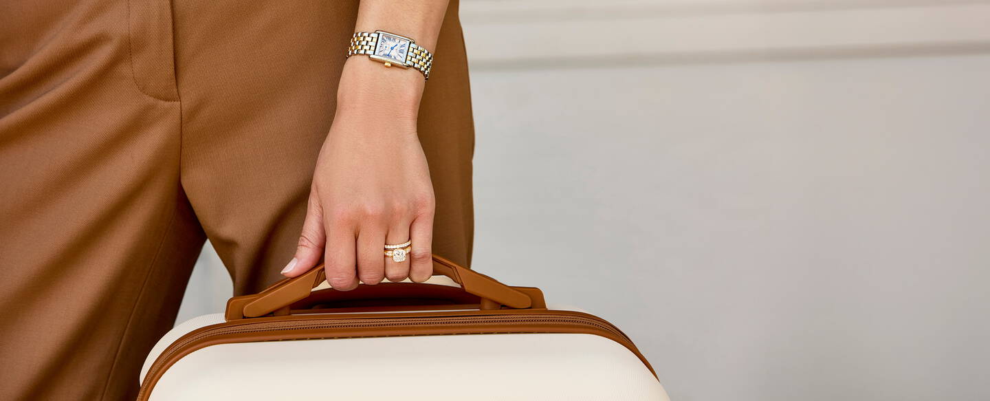 A woman&rsquo;s hand holding a brown and cream colored suitcase.