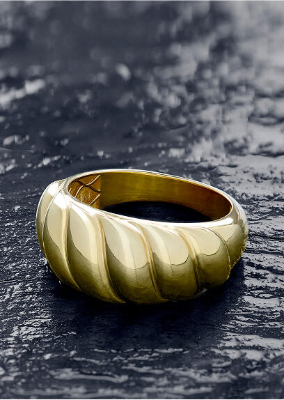 A fluted yellow gold ring on a shiny black surface.