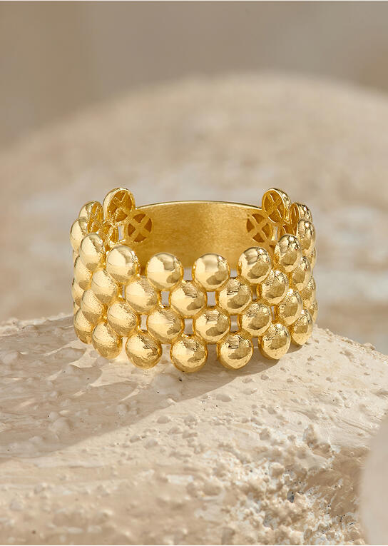 A four-row beaded ring crafted in 14k yellow gold casts a shadow on a stone surface. 