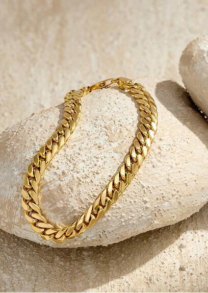 A yellow gold bracelet is draped over a stone.