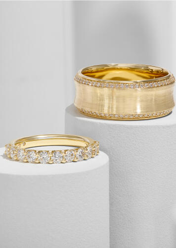 Two diamond wedding bands set in yellow gold atop small cylindrical podiums.