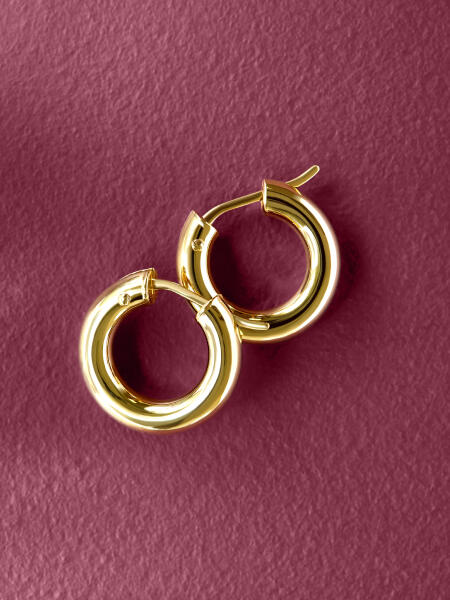 A pair of yellow gold hoop earrings lay side by side on a purple surface. 