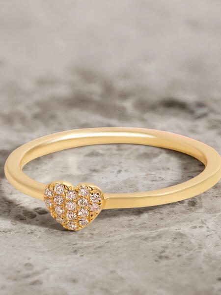 A heart-shaped yellow gold ring with a diamond cluster lays on a gray marble surface.