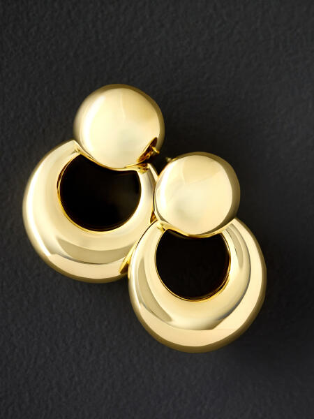 A pair of yellow gold doorknocker earrings shine against a gray backdrop.
