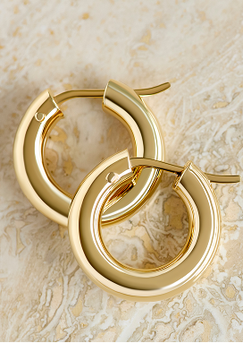 Classic hoop earrings crafted in 14k yellow gold shine on a smooth marble surface