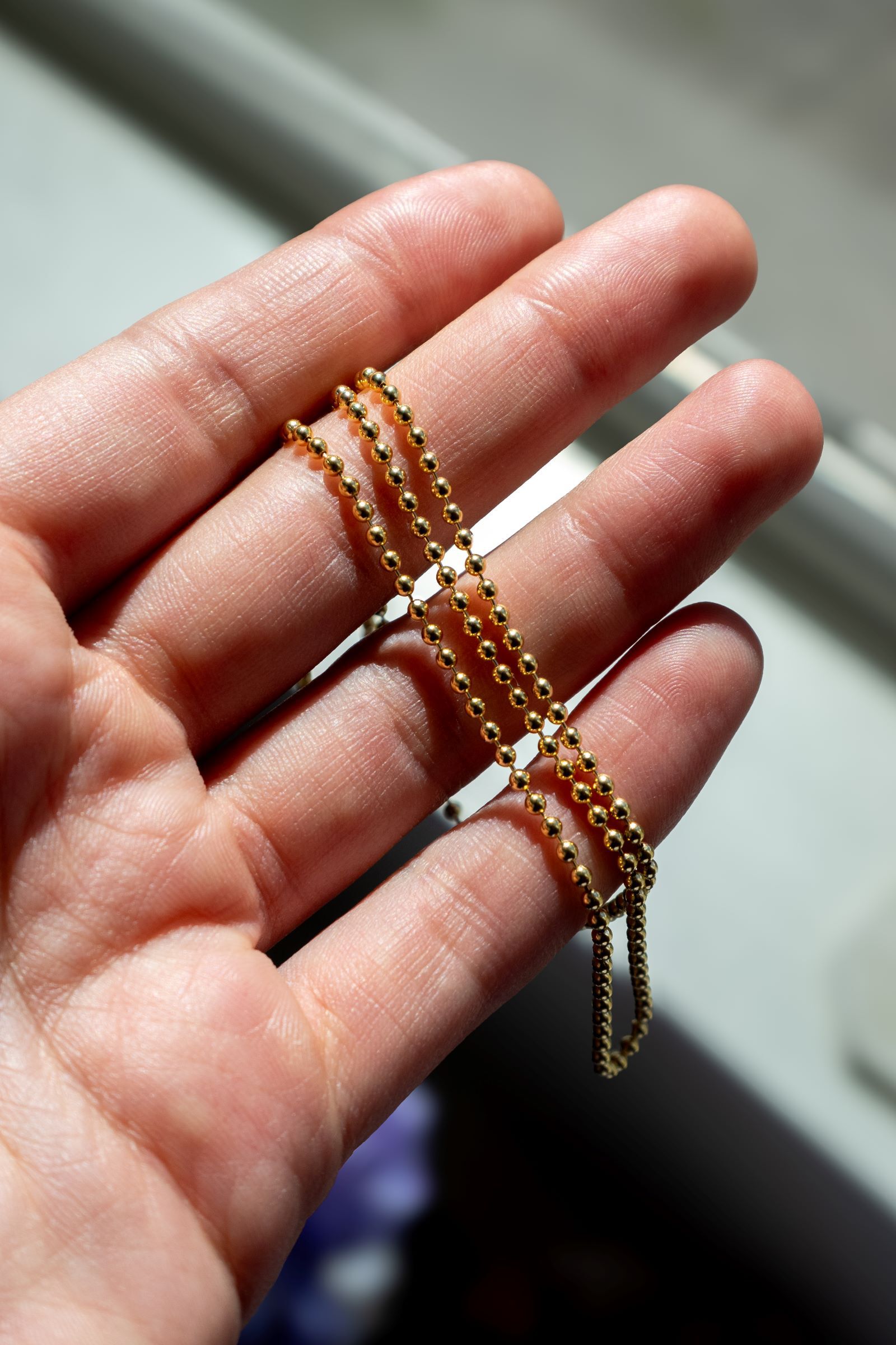 A yellow gold beaded necklace draped over a woman's fingers A yellow gold beaded necklace draped over a woman's fingers