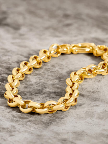 A bold yellow gold bracelet rests on a smooth marble surface of varying shades of gray.&nbsp;