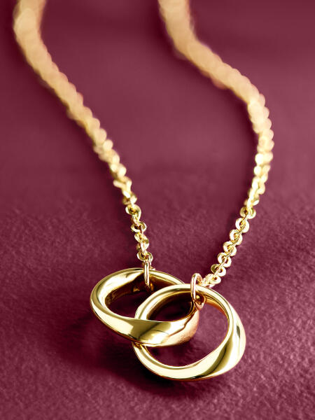 A yellow gold necklace features a centerpiece of interlocking gold hoops and shines on a purple background.