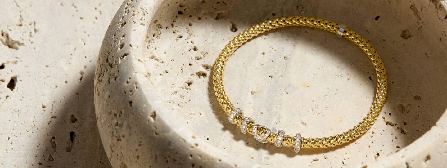 A yellow gold bracelet with a beaded texture features diamond accents set in white gold. 