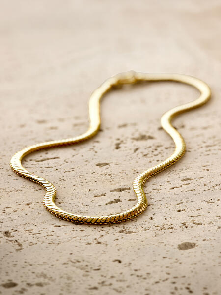 A Classic yellow gold necklace rests on a porous stone surface.