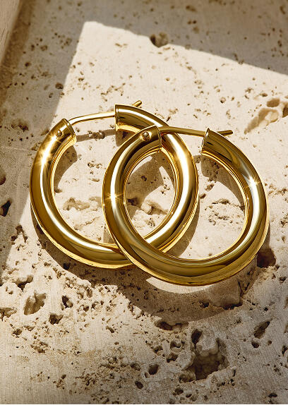 A pair of yellow gold hoop earrings overlap and are cast in light amid angular shadows.