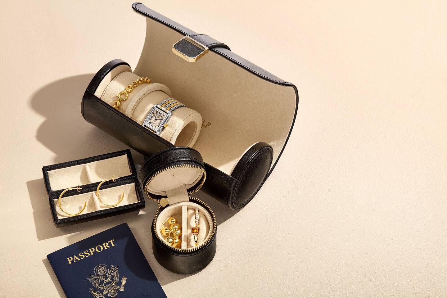 A watch and bracelet inside a travel watch roll alongside jewelry and a passport