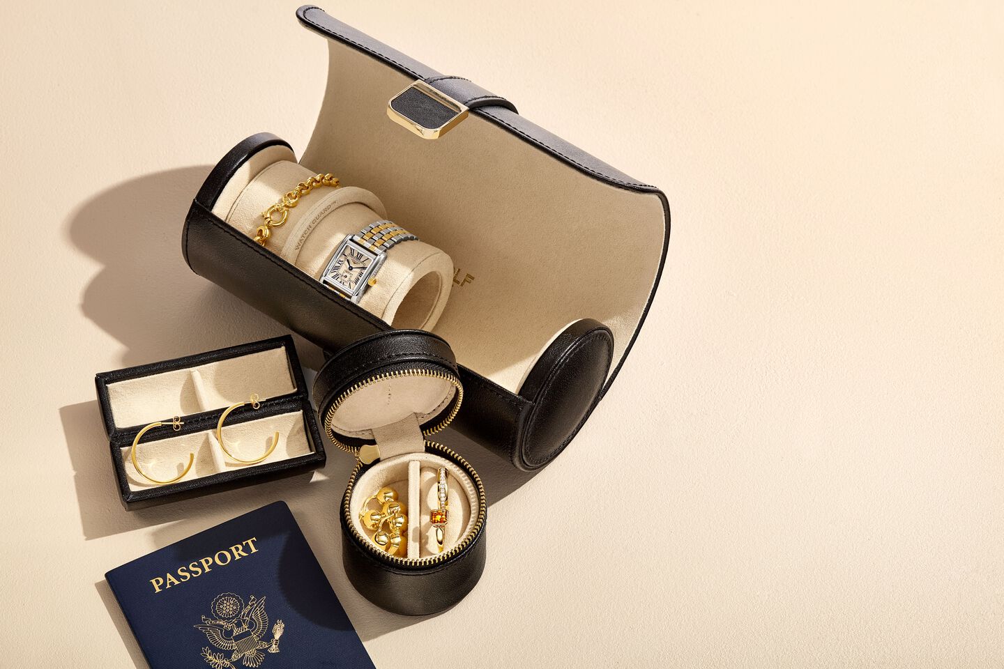A watch and bracelet inside a travel watch roll alongside jewelry and a passport