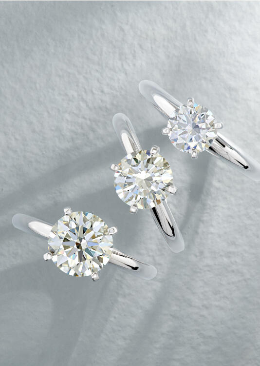 Three solitaire diamond engagement rings cast a shadow against a textured white background.