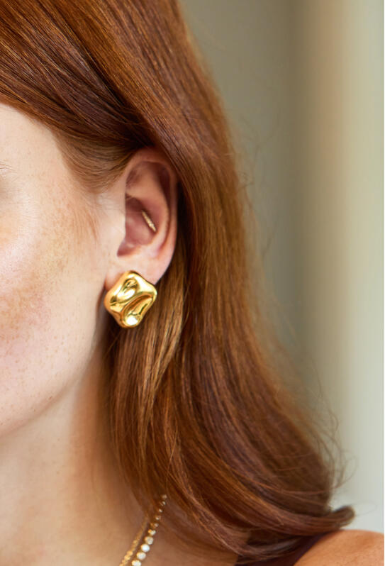 Closeup of a woman’s ear highlights the yellow gold studs she is wearing.