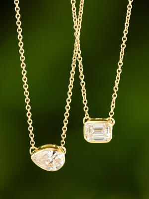 Two solitaire diamond pendant necklaces set in yellow gold against a green background.