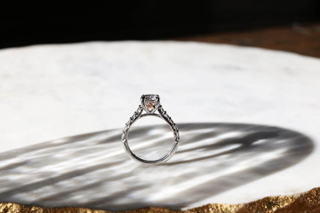 A diamond solitaire ring in white gold is balanced on a white surface