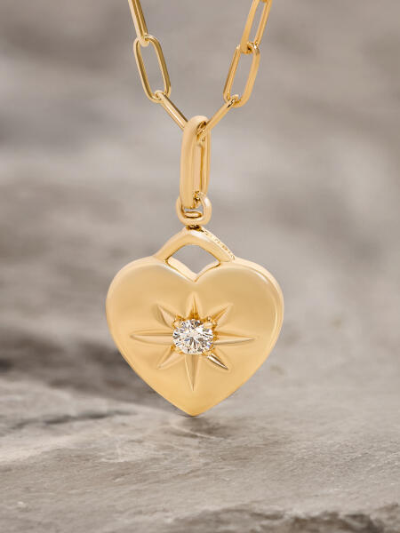 A yellow gold heart-shaped pendant on a gold chain features a single round diamond in the center.