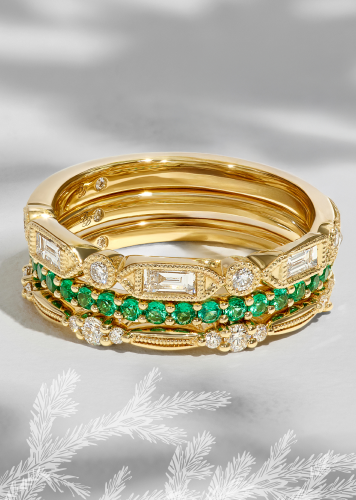 A stack of anniversary bands with diamonds and green colored gemstones, all set in yellow gold