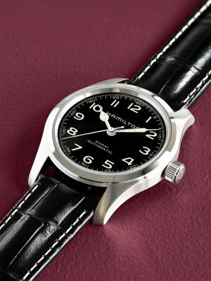 Field watch with a black dial and leather strap on a purple background.