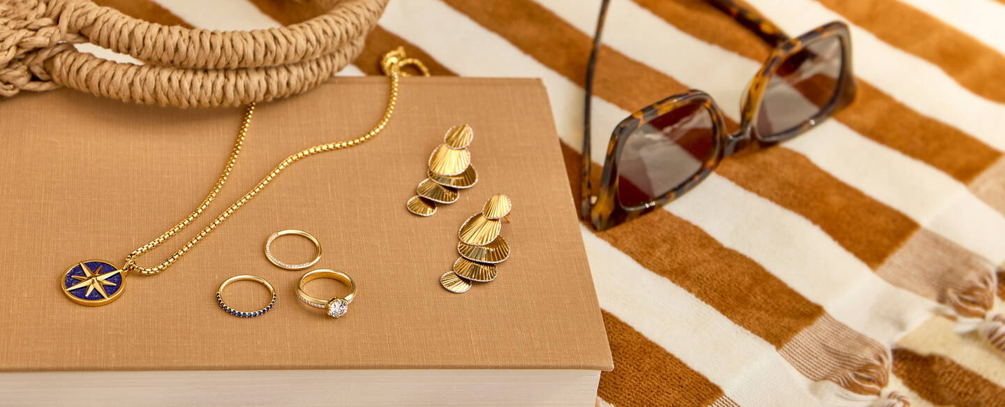 Gold and gemstone jewelry rests on a book on a striped beach towel.