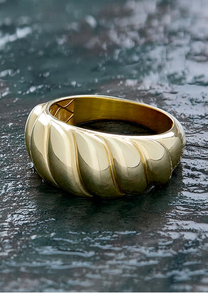 A fluted yellow gold ring on a dark stone surface