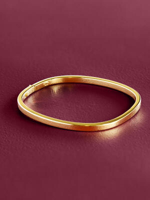 A yellow gold bangle rests on a purple surface.