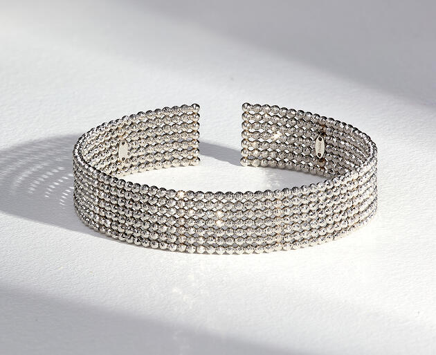 A platinum bracelet with several rows of diamond cut beads casting a shadow across a smooth light gray surface.