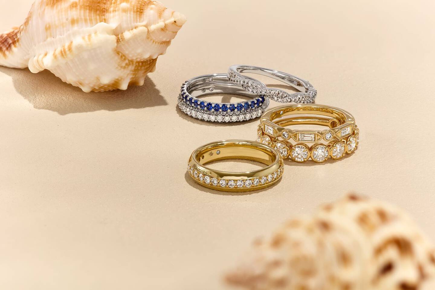 diamond and colorful gemstone rings on beach sand with seashells