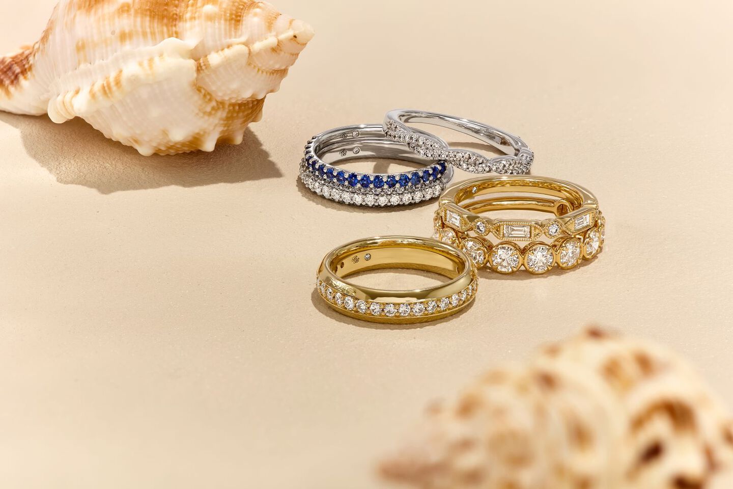 diamond and colorful gemstone rings on beach sand with seashells