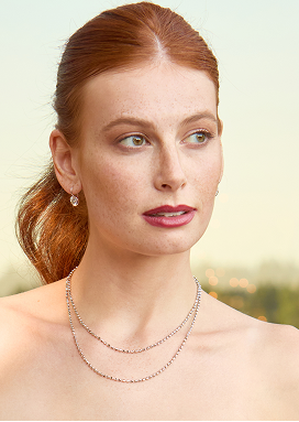 A woman gazes toward the distance. Her hair is tied back and she is wearing a diamond necklace.