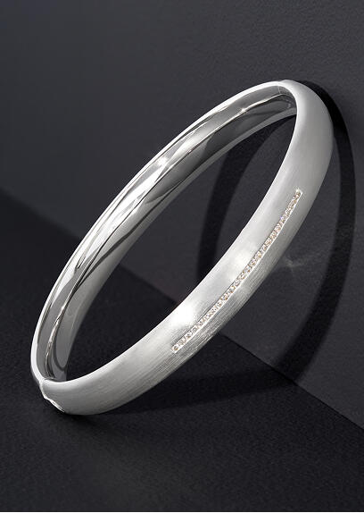 A white gold bracelet leans against the corner of a gray surface