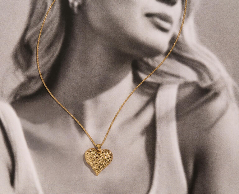 Black and white photo of a woman gazing peacefully toward the horizon. The only item in color is a yellow gold necklace with a heart-shaped pendant.