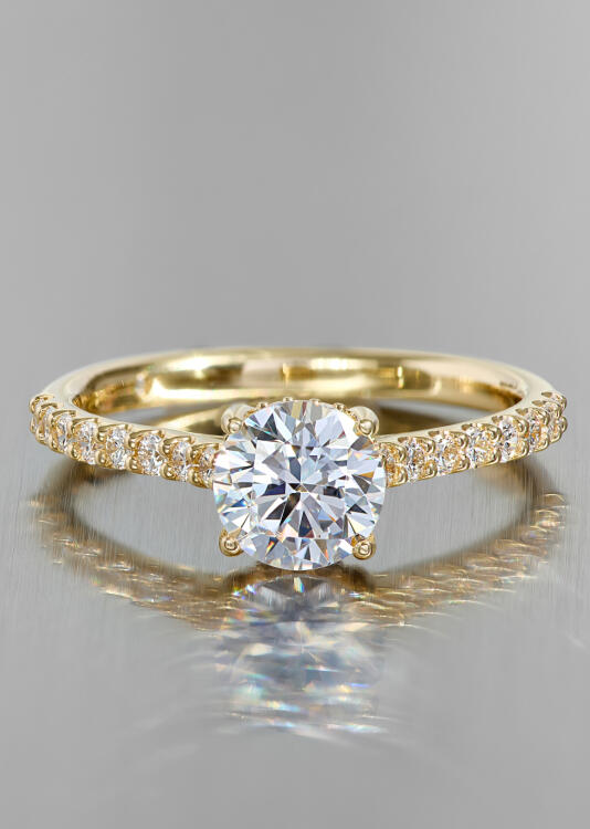 A round diamond engagement ring in yellow gold with accent diamonds along the shank.
