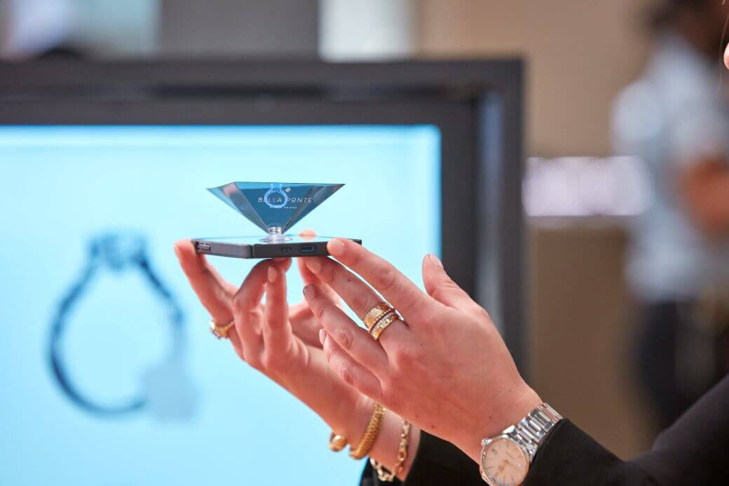 A woman hold up a hologram rendering of a custom engagement ring to demonstrate the mobile technology available