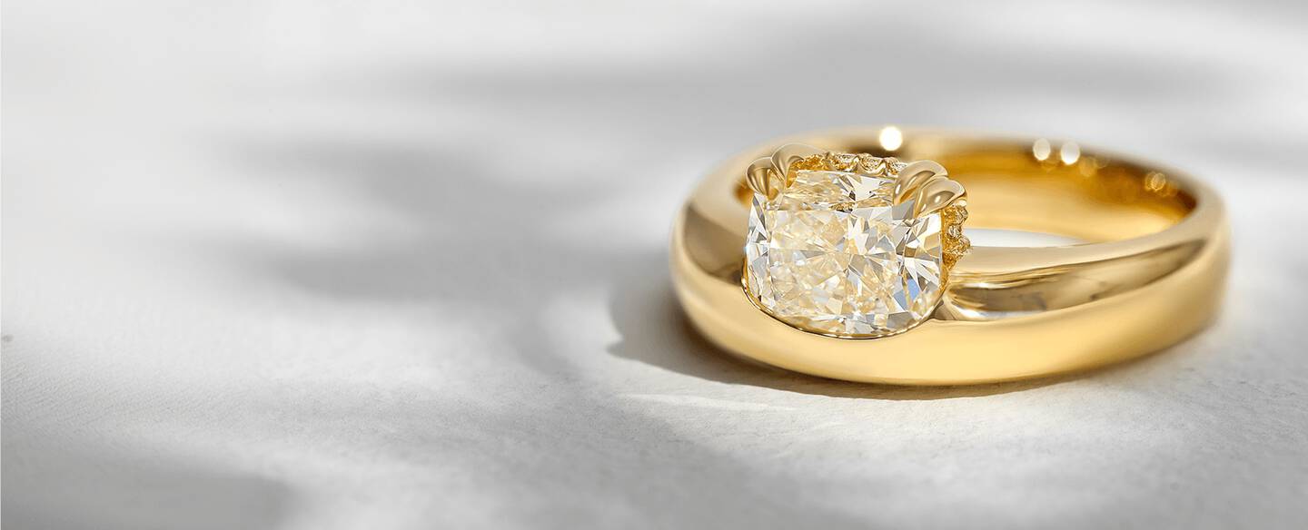 A solitaire diamond ring with an off-centered primary stone in a prong setting of yellow gold. 