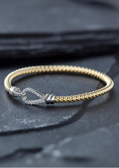 A yellow gold bracelet features diamond accents and rests on a dark stone surface