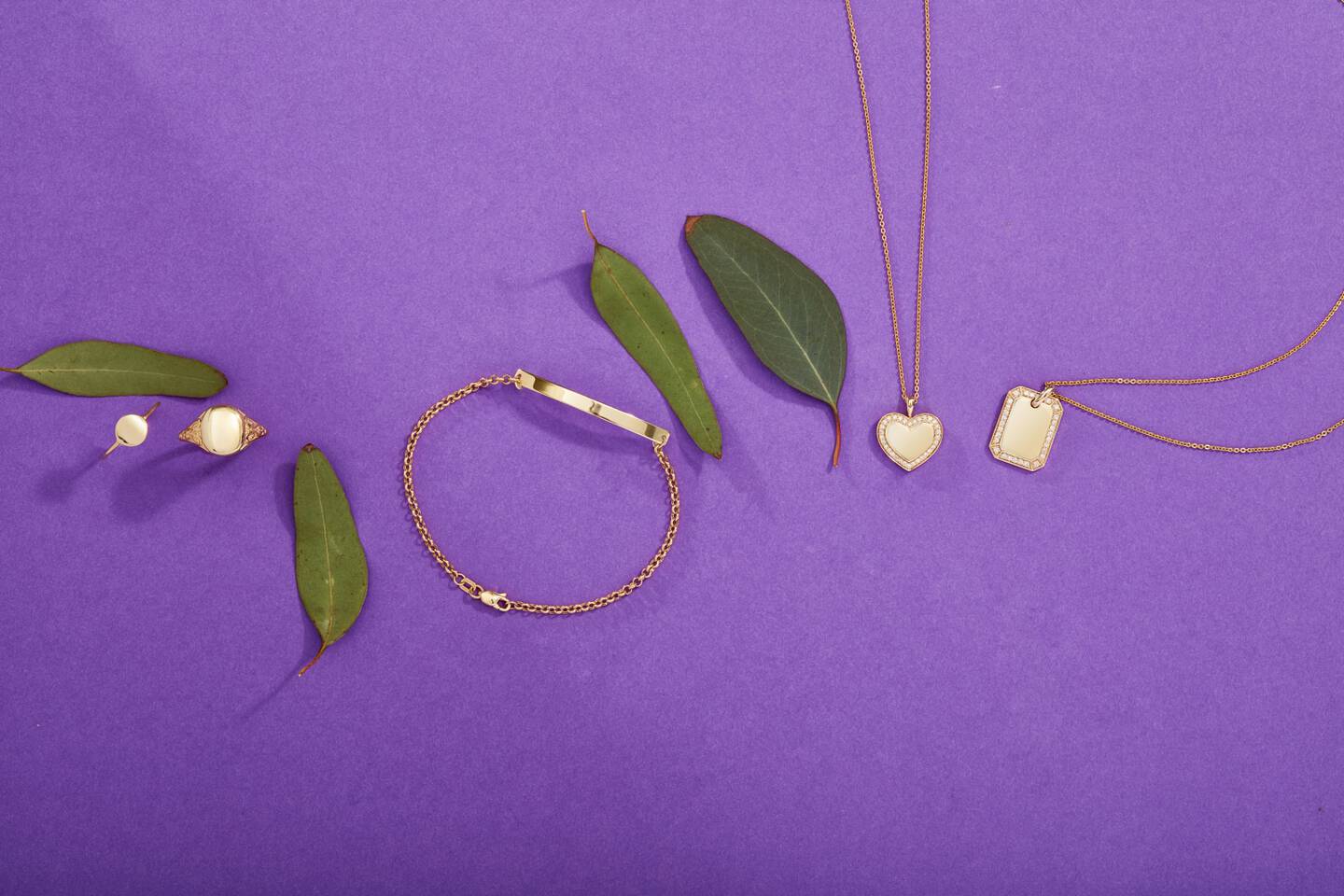 Engravable gold bracelets, rings and necklaces shine against a purple background