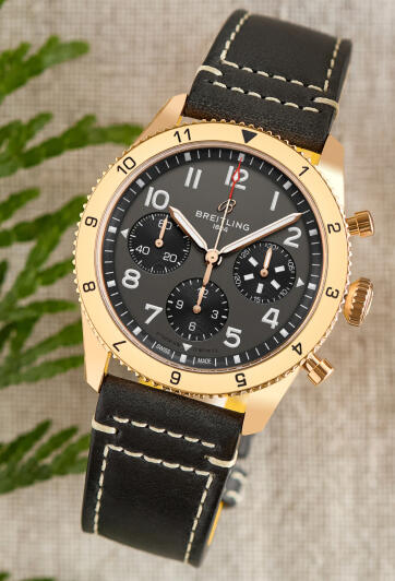 Breitling chronograph watch with a gold case and black dial against a textured backdrop.