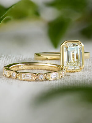Diamond wedding band and engagement ring set in 14k yellow gold shine against a blurred background.