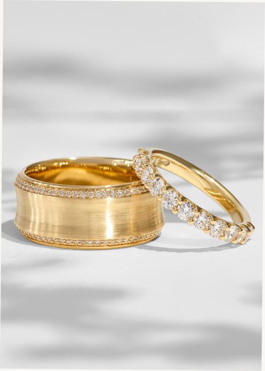 Two yellow gold wedding bands of varying widths and texture, both featuring natural round diamonds. 