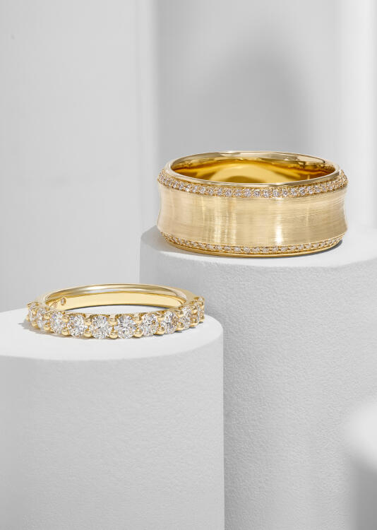 A yellow gold band in a satin finish features a perimeter of round diamonds while a diamond anniversary ring sparkles alongside it.
