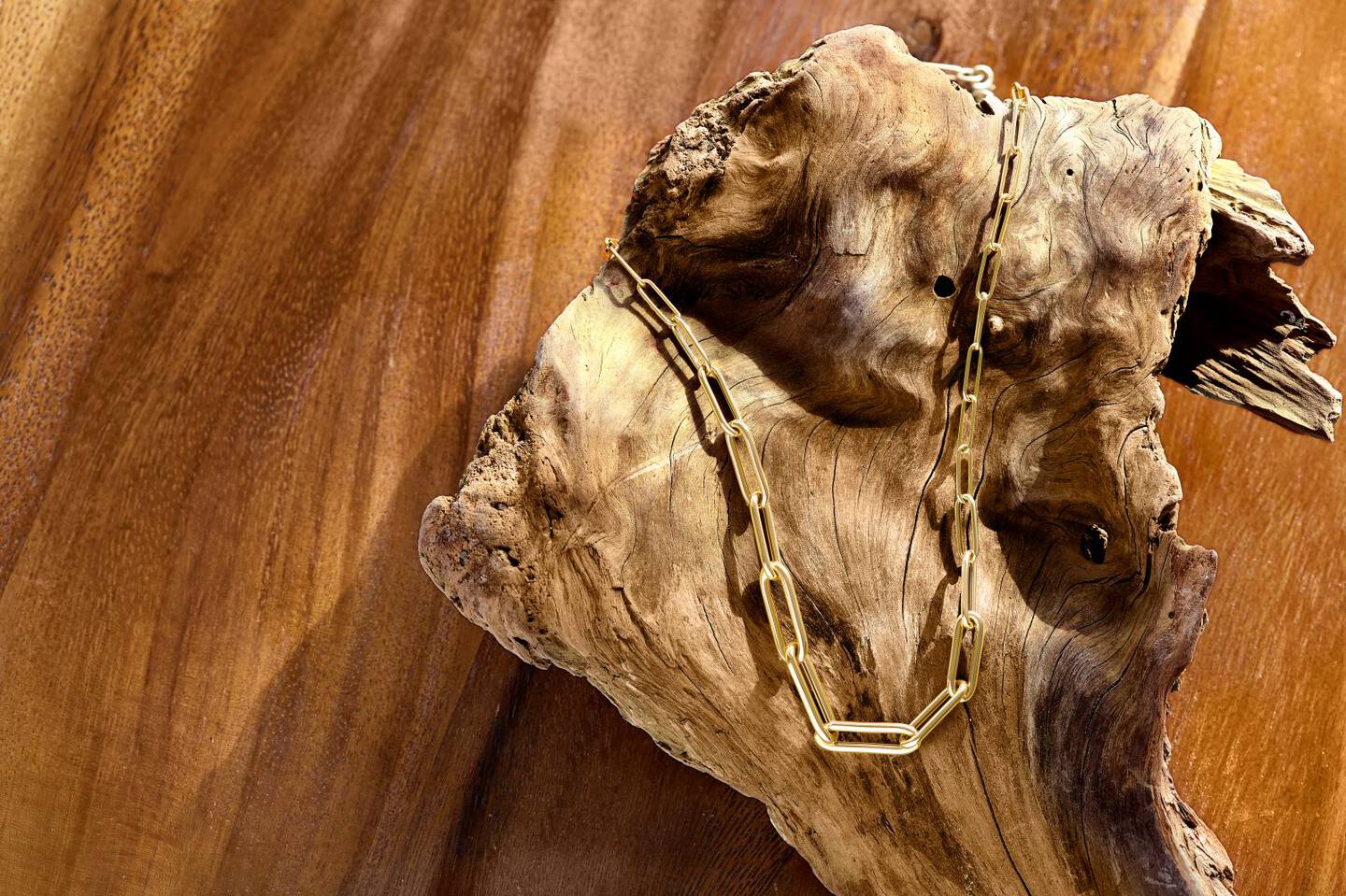 A yellow gold paperclip chain is draped across a woman's fingers