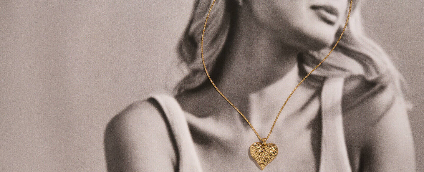 Black and white photo of a woman gazing peacefully toward the horizon. The only item in color is a yellow gold necklace with a heart-shaped pendant.