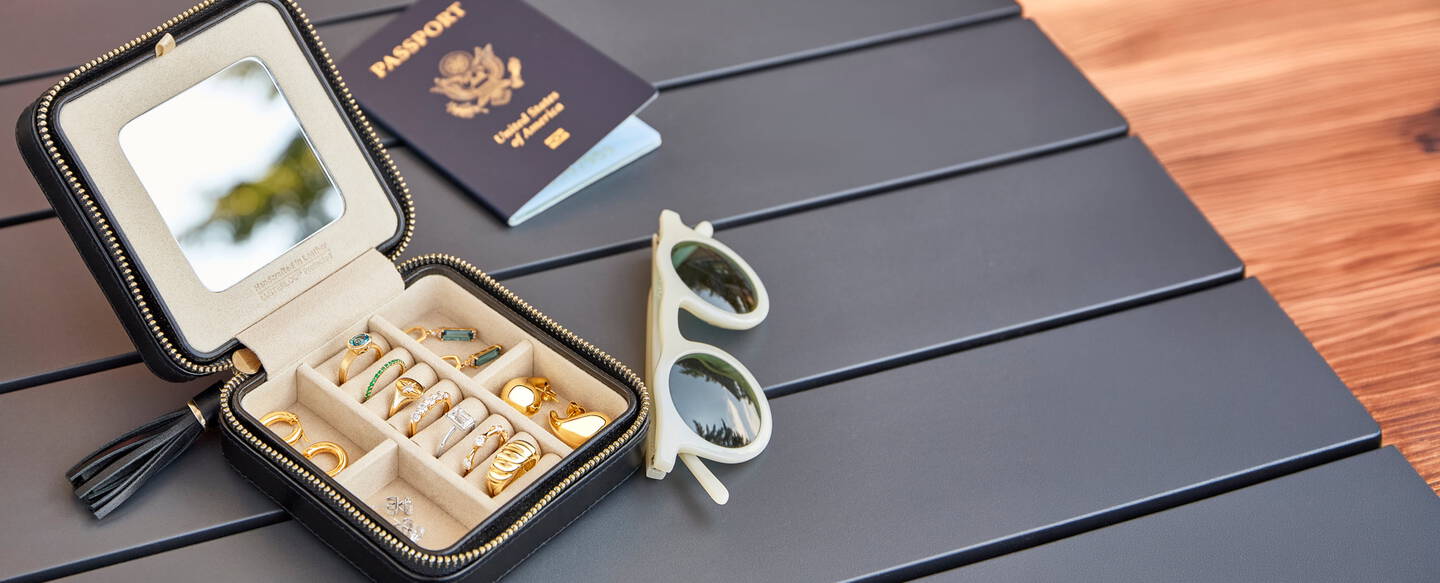 Tabletop with a jewelry case with jewelry inside, a passport and pair of sunglasses.