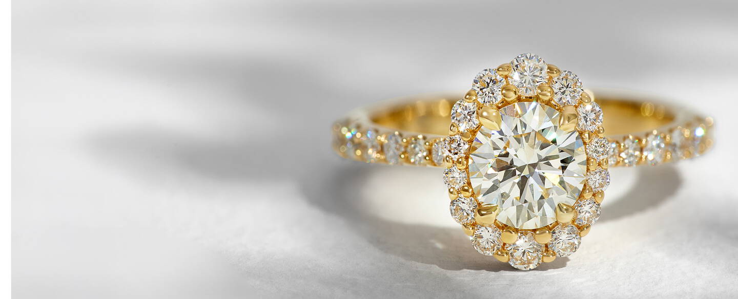 A round diamond engagement ring with a diamond halo and accent diamonds along the yellow gold shank.